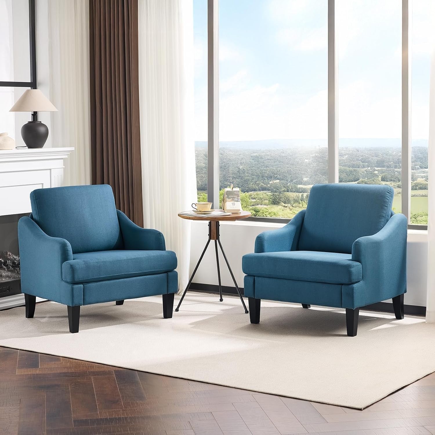 Two teal-blue upholstered armchairs arranged with a tripod side table in front of large windows.