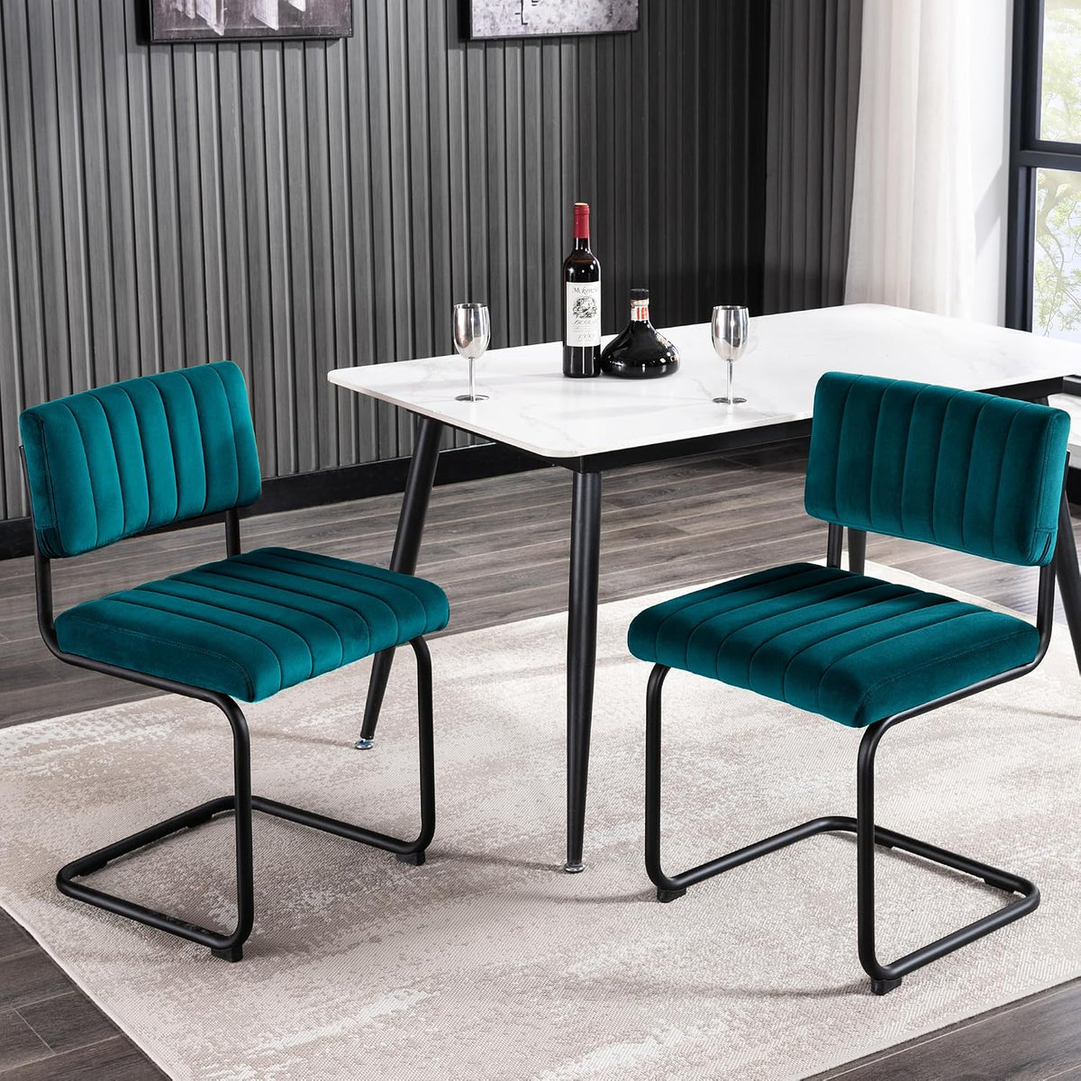 Low-angle view of two teal velvet cantilever chairs at a white tabletop with a wine bottle and two glasses