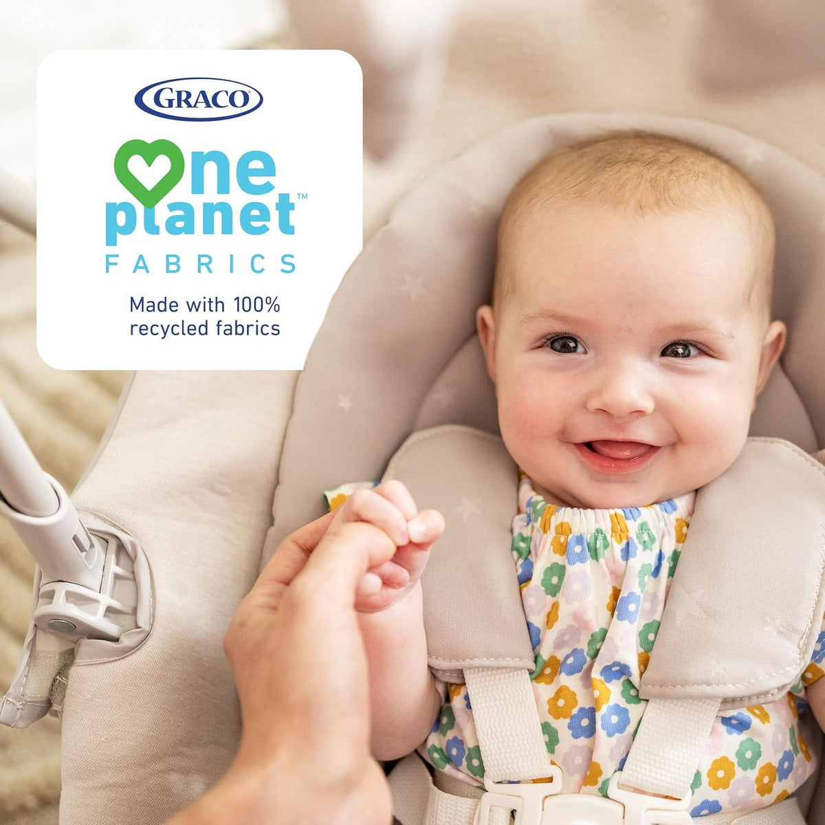 close-up of a smiling baby seated in a padded highchair holding an adult's finger