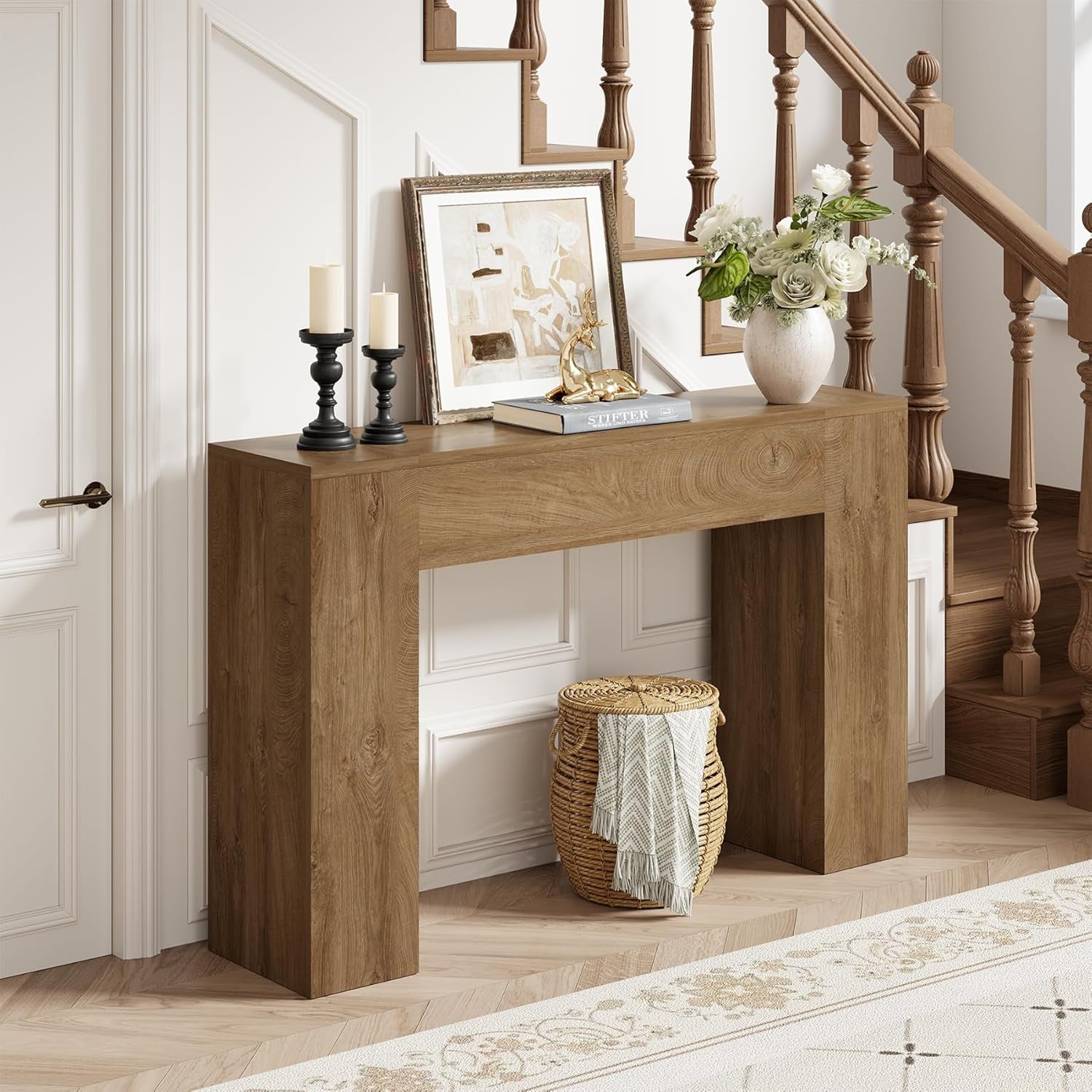 Light oak console table in an entryway setting with vase, framed picture and woven basket below