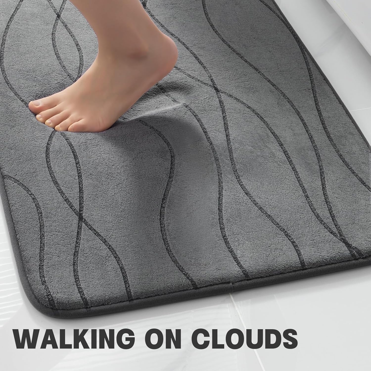 Foot pressing into dark grey memory foam rug showing cushioning and raised wave pattern, close-up view