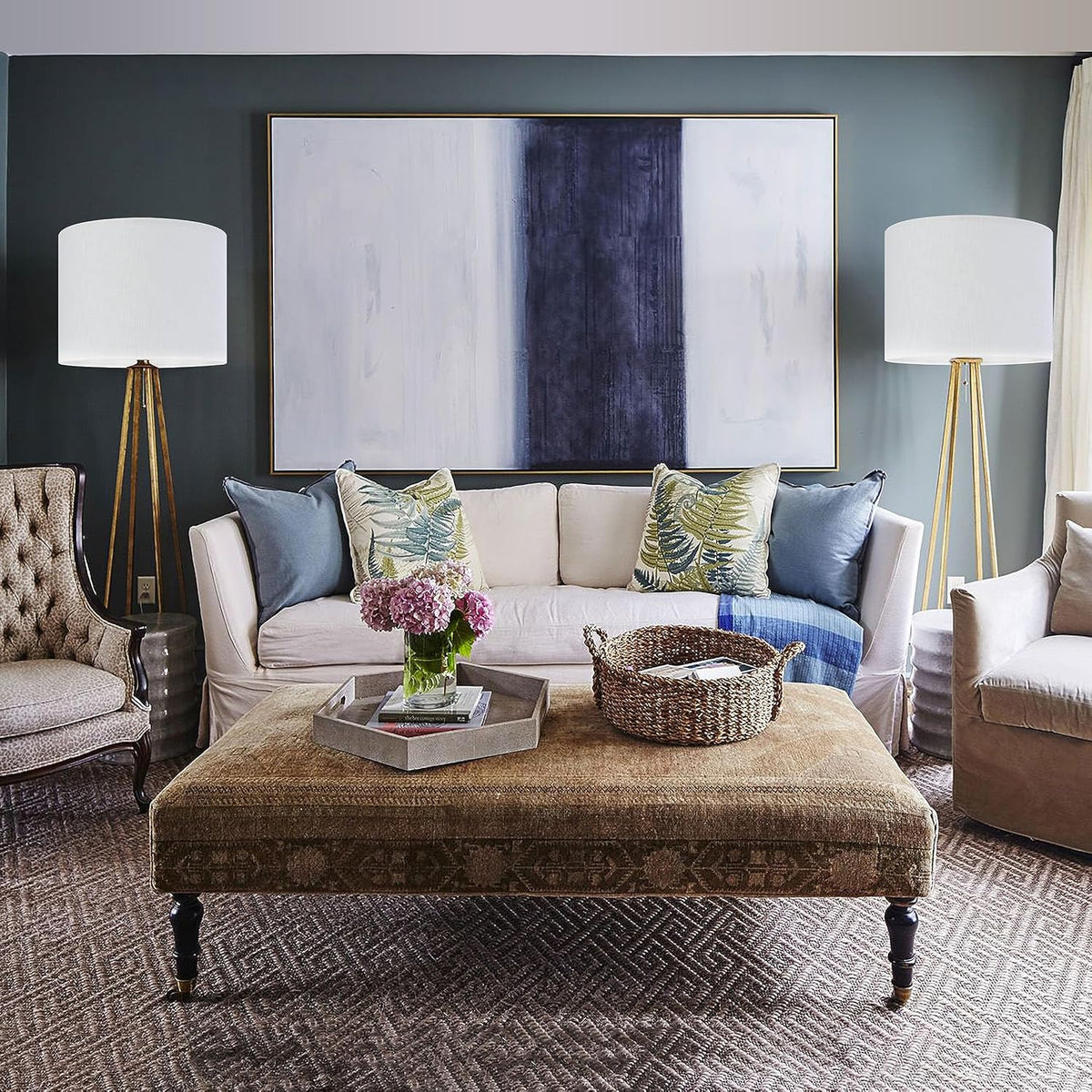 Living room scene with a sofa and two white drum lamp shades on tripod floor lamps flanking a painting.