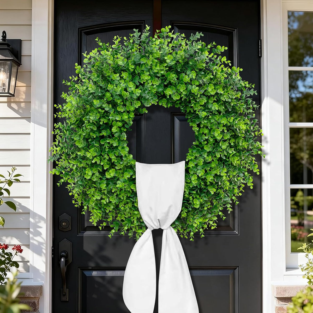 Green boxwood wreath hung on a black front door with a white sash