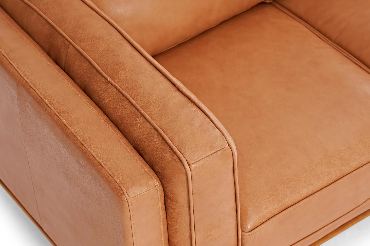Top-down view of a cognac leather sofa showing armrest, seat cushion, and stitched piping.