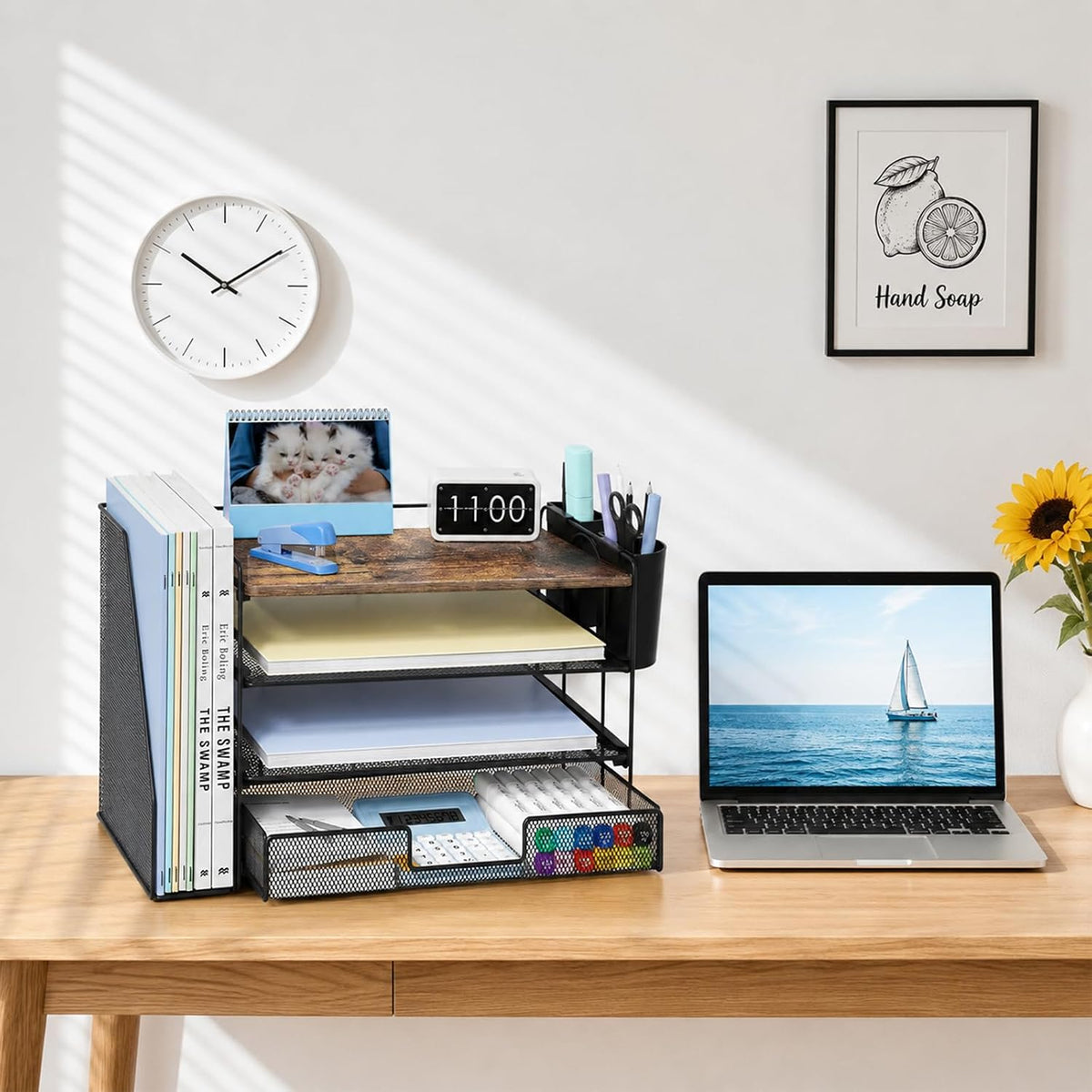 Desk with black 4-tier mesh file organizer beside a laptop, clock and sunflower vase