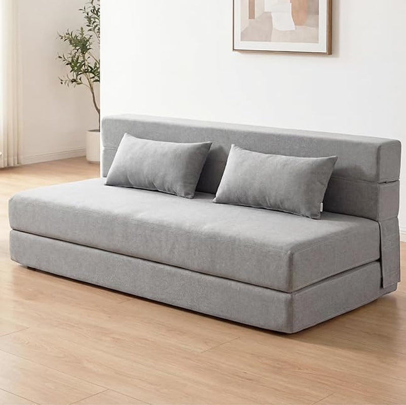 Light-gray sofa bed placed on wood floor against a white wall with two pillows