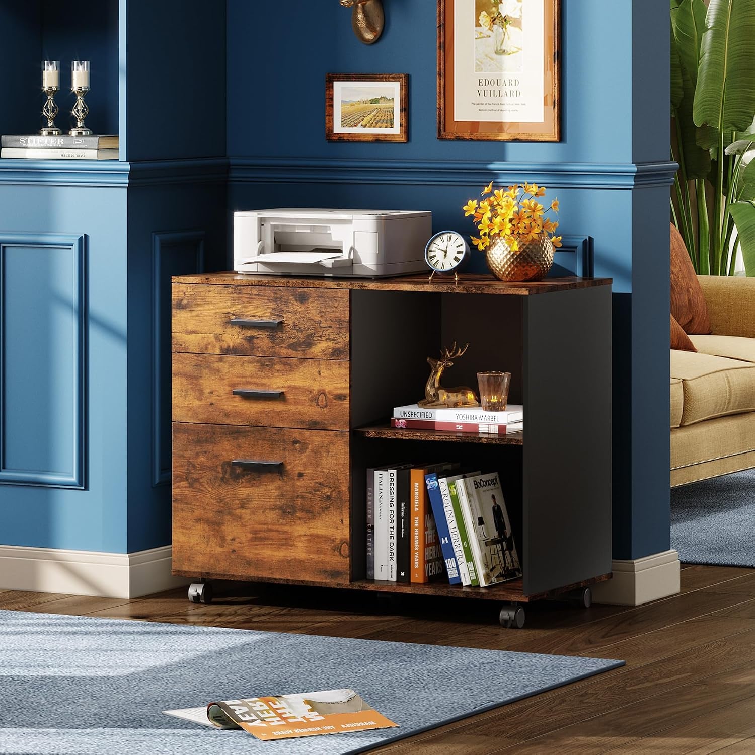 Cabinet placed against a blue wall beside a sofa with a printer and decorative items on top and books on its open shelf.