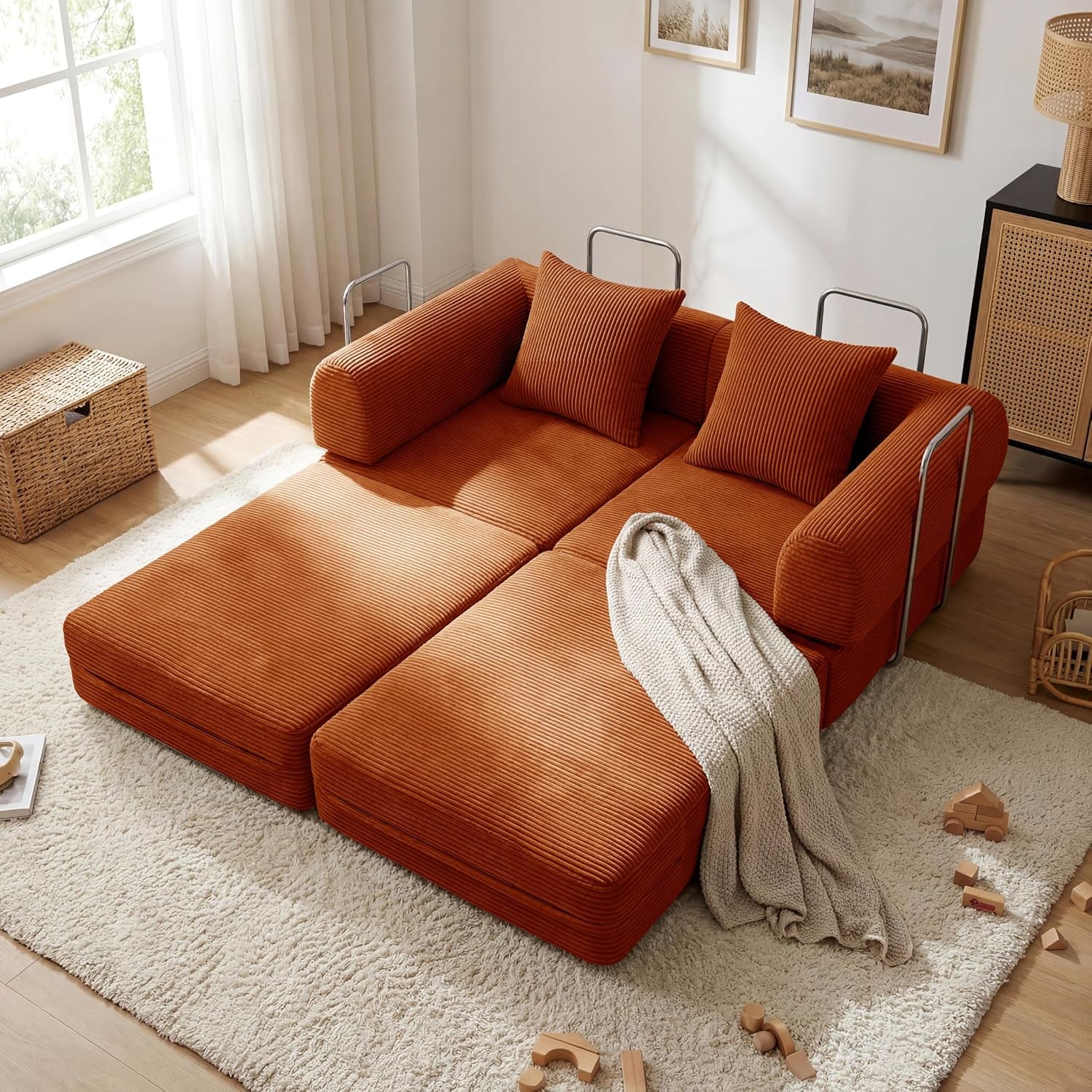 Orange corduroy sofa unfolded into a low double-bed layout with pillows and a throw.
