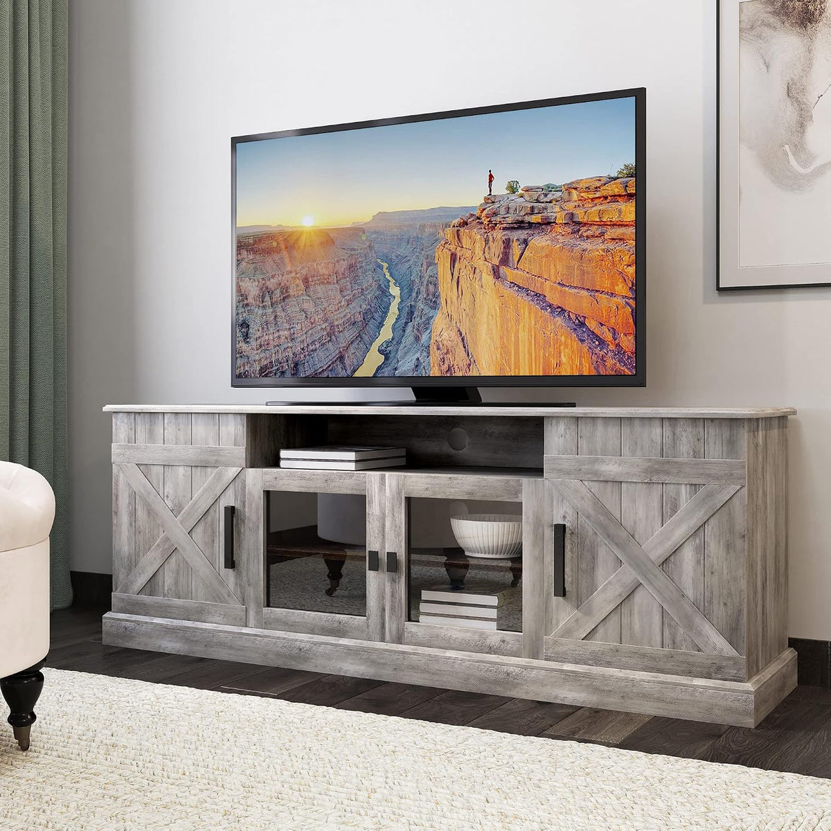Front-facing crop of a gray-wash farmhouse TV stand with a large TV, glass center doors and open shelf.