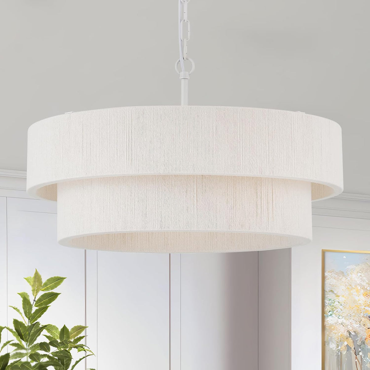 White three-layer drum pendant shown in a neutral room with a plant and framed artwork