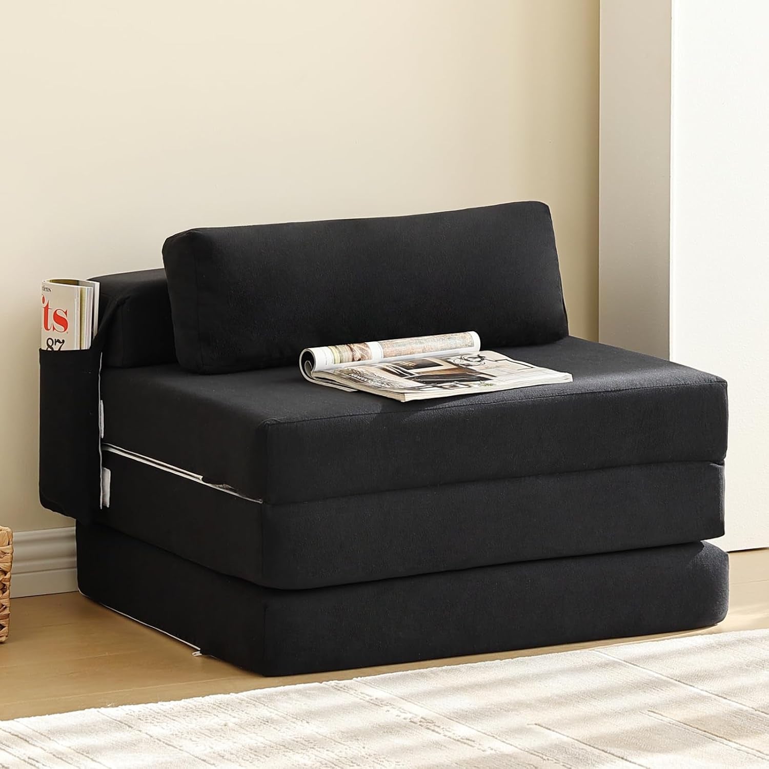 Black foldable sofa bed chair with pillow and side pocket styled with a magazine on top.
