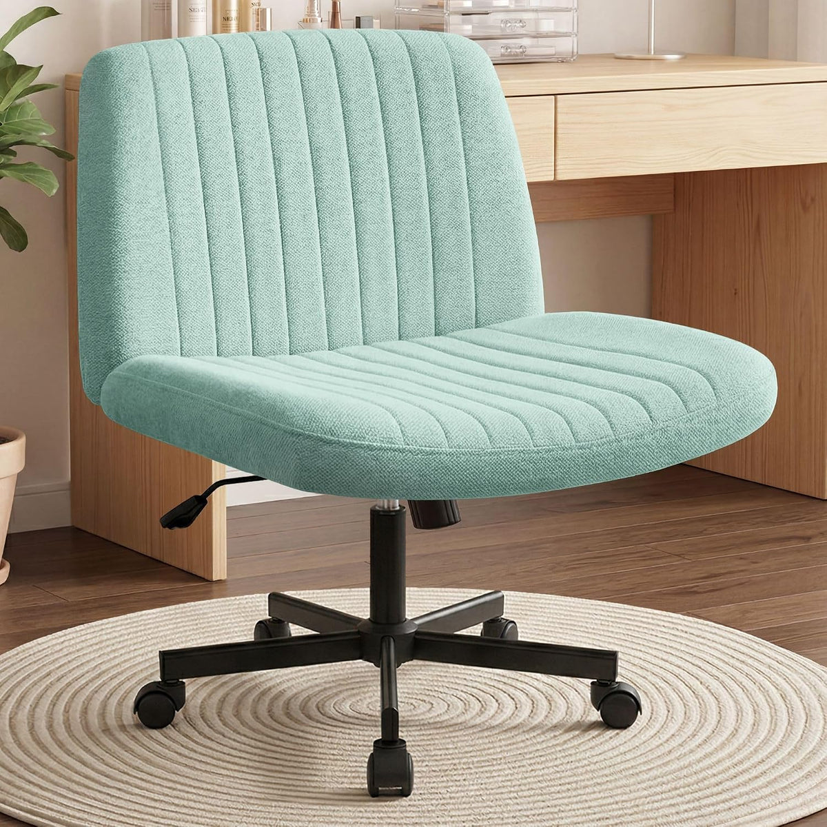 Seafoam green upholstered desk chair with stitched vertical channels and black base beside a wooden desk.