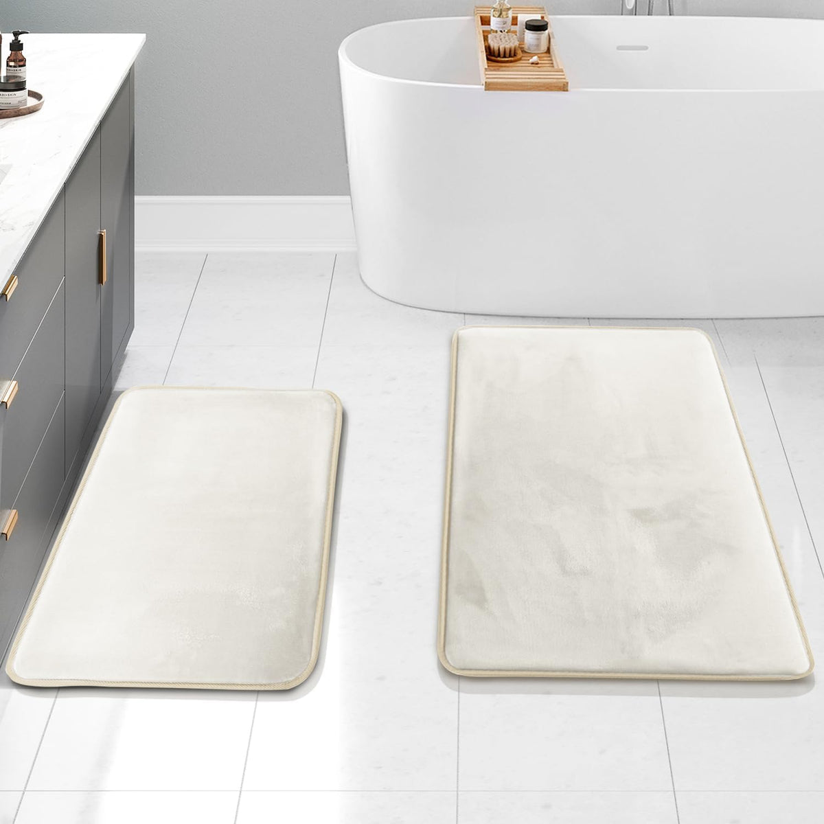 Overhead view of two ivory bath rugs laid on a tiled floor in front of a tub and vanity