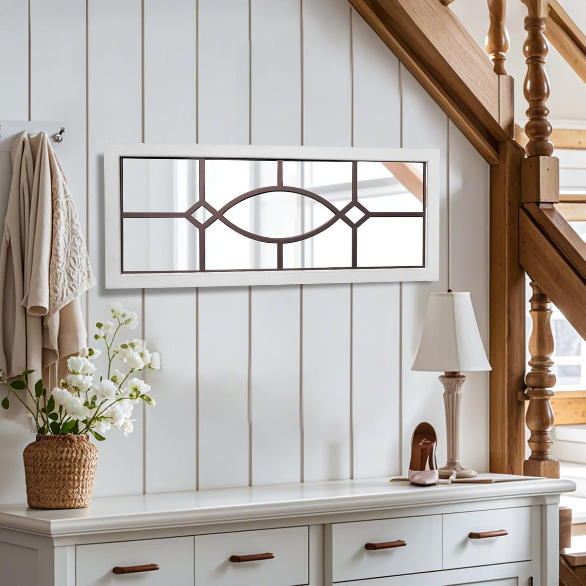Wide white framed windowpane mirror with brown inner pattern mounted on a light-paneled entry wall beside stairs.