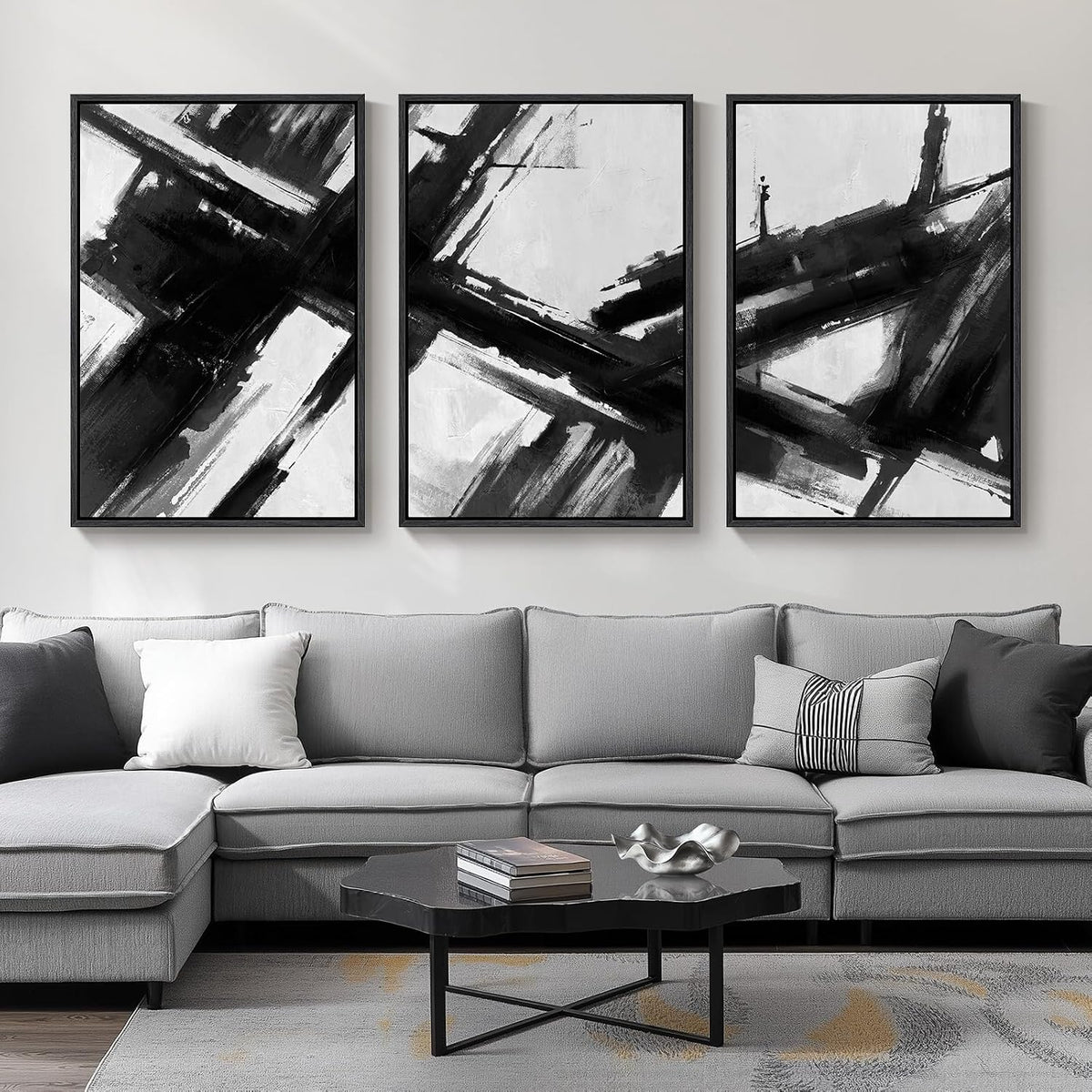 Three black-and-white framed abstract canvases with bold brushstrokes hung above a gray sectional sofa and coffee table.