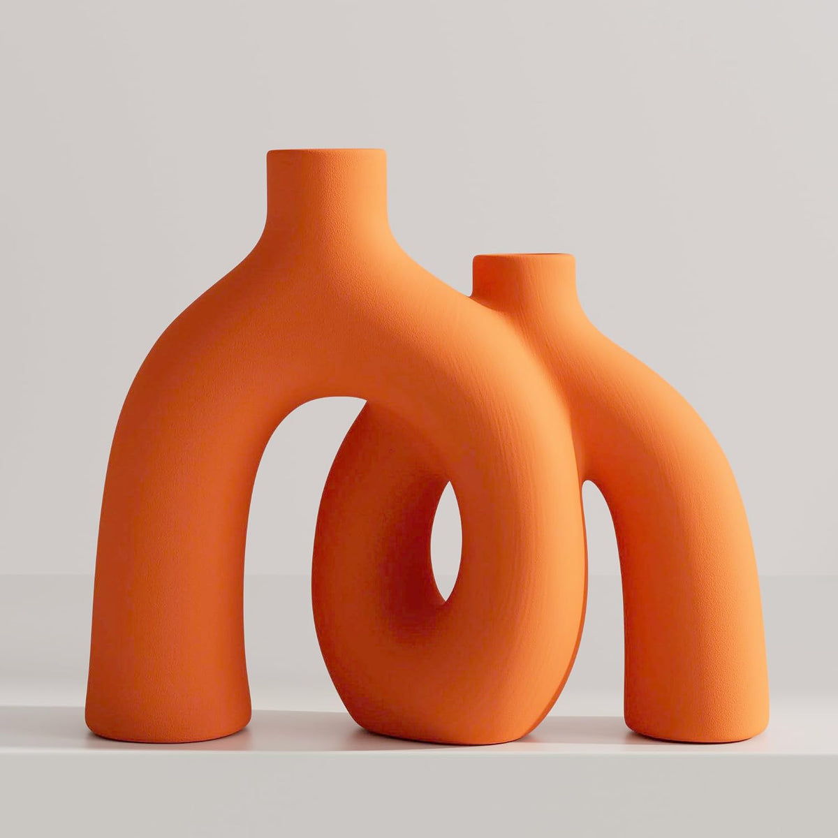 Two interlocking donut-shaped ceramic vases in matte orange on a white surface