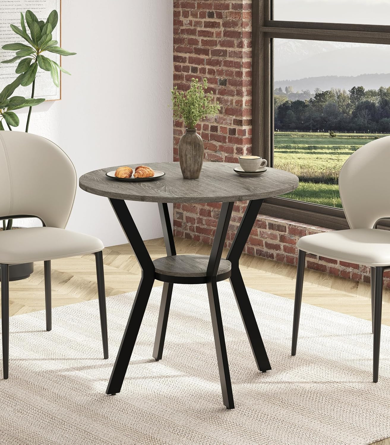 Round gray wood-look table with black angled legs and center shelf, shown between two chairs.