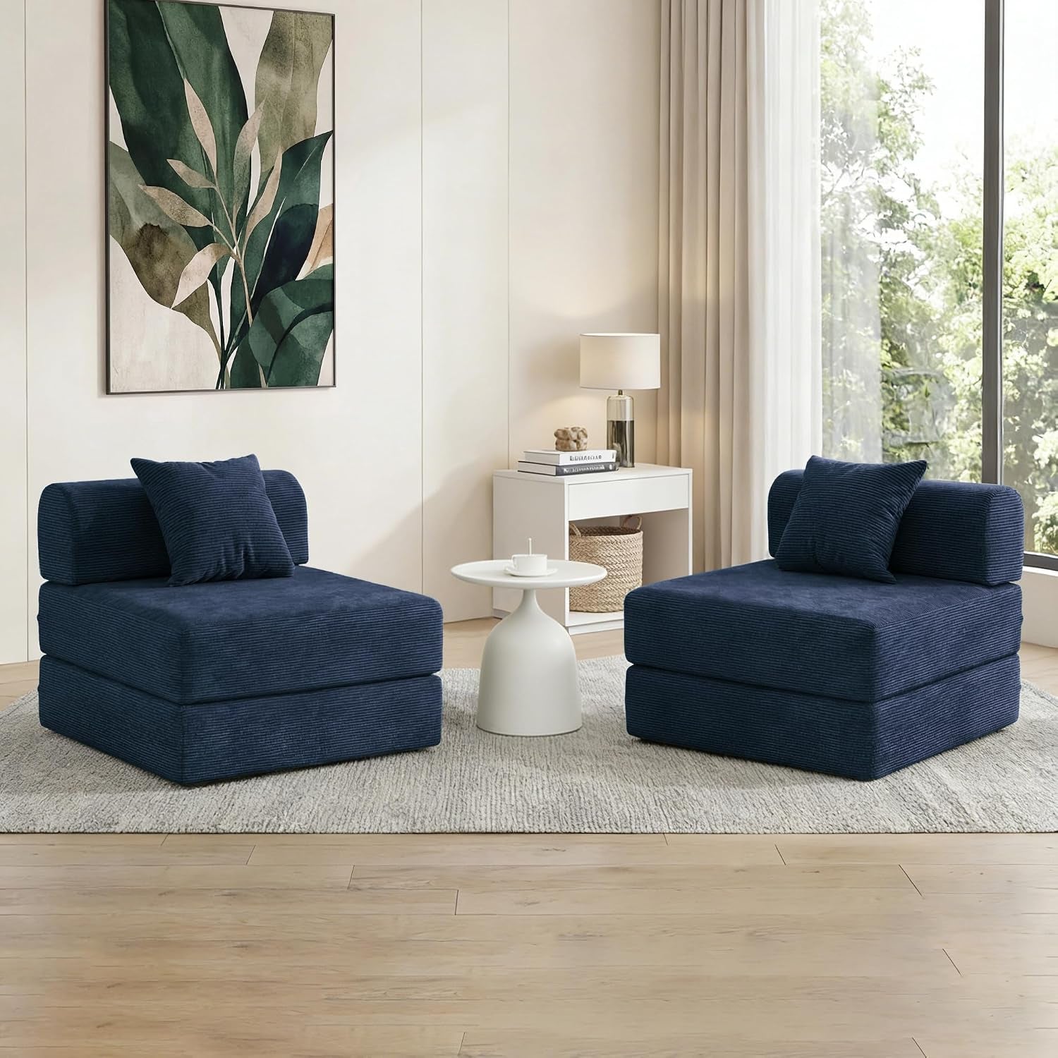 Two navy corduroy armless lounge seats with matching pillows flanking a small white side table in a bright room