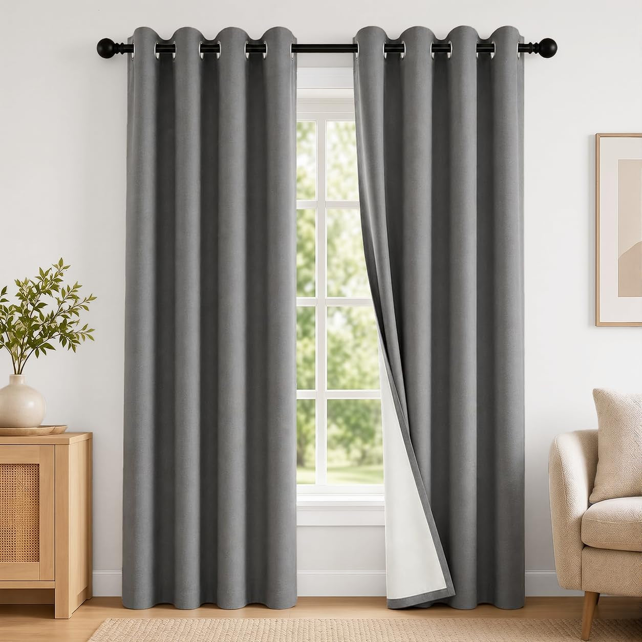 Charcoal grey blackout curtain panels framing a window in a living room with a side table and armchair visible.
