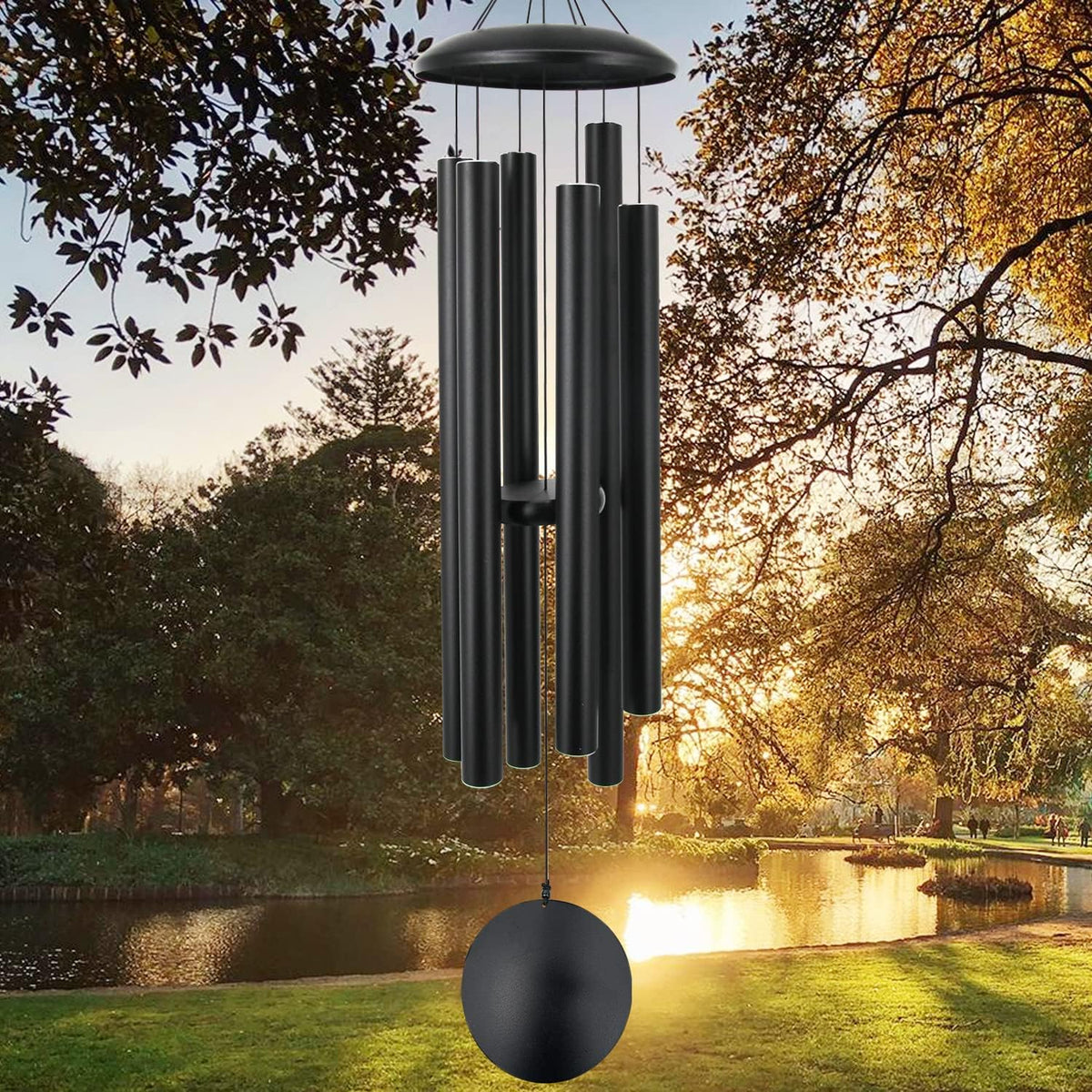 Wind chime hanging outdoors over a pond at sunset with trees and golden light in the background.