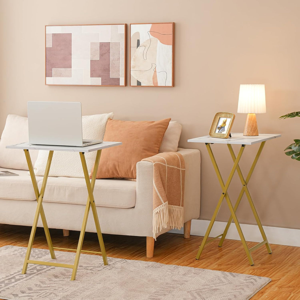 Pair of marble-pattern tray tables beside a beige sofa with a laptop and lamp on the tops