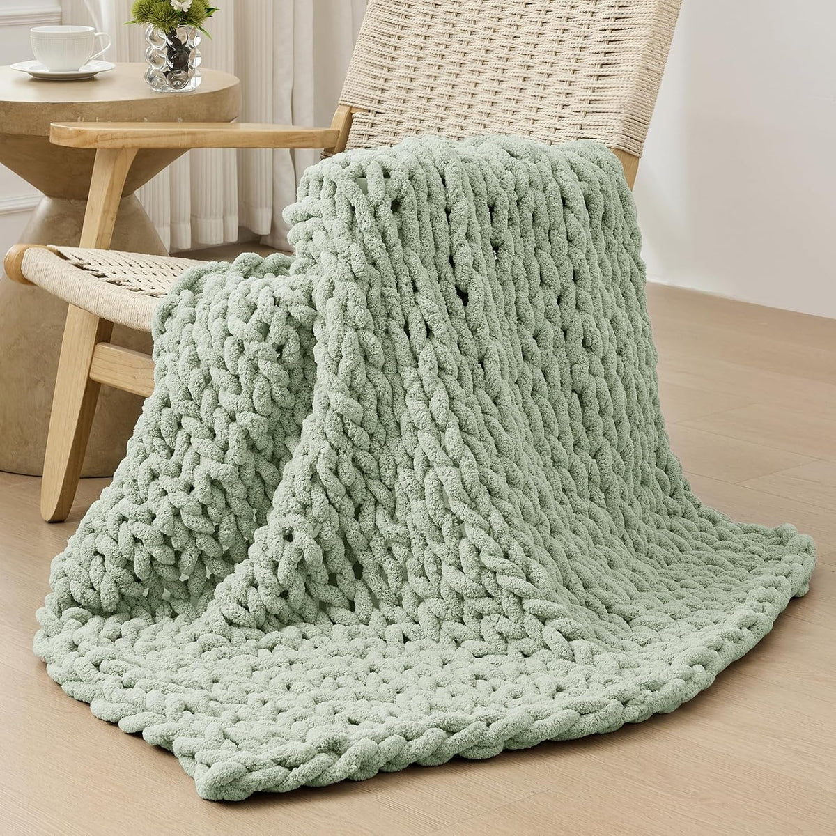 Pale mint-green chunky throw draped over a woven lounge chair with a round side table in background