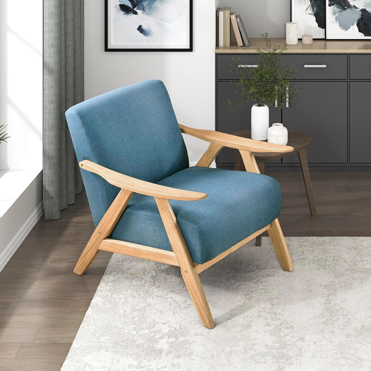 Blue upholstered mid-century accent chair with light wooden frame positioned on a rug near a window