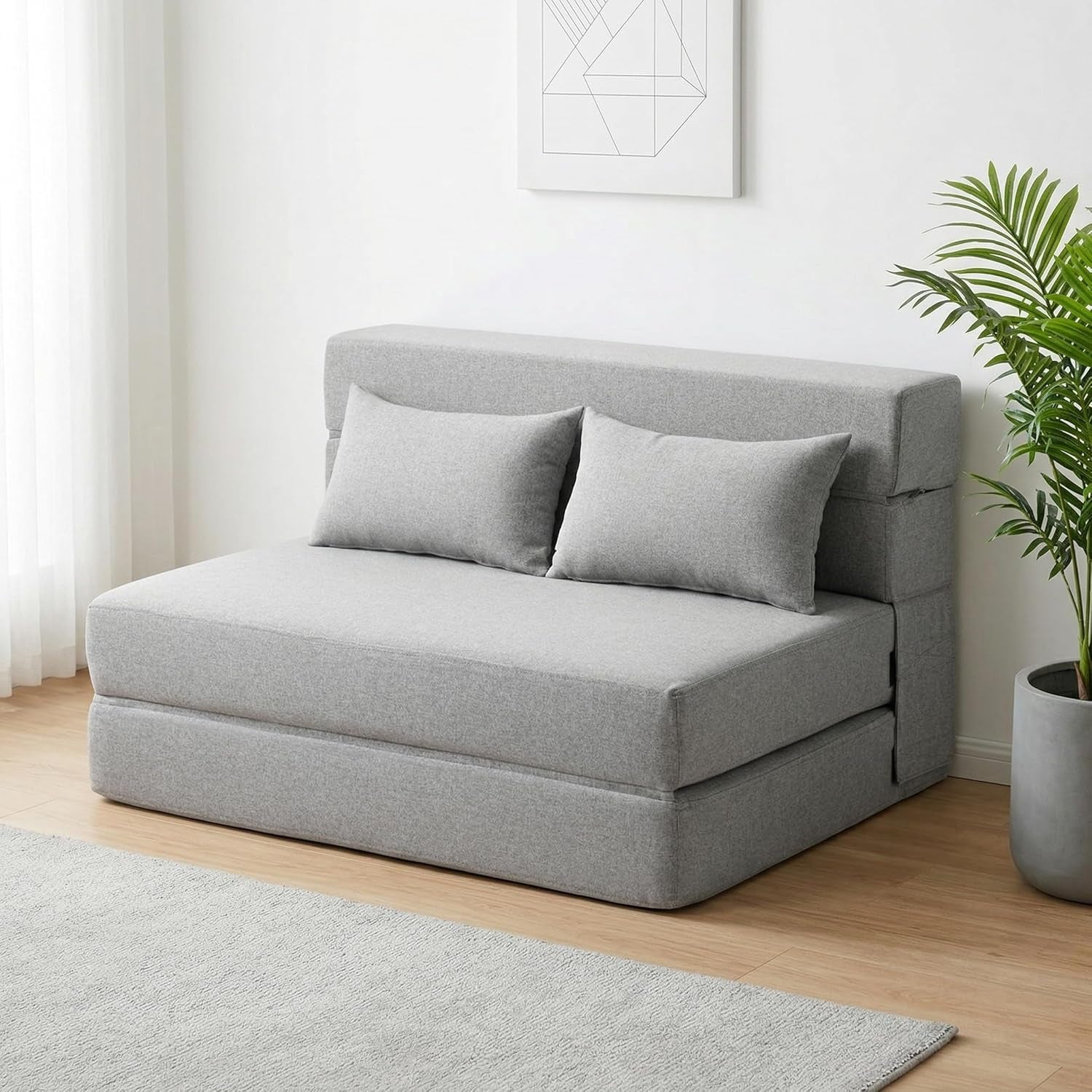 Light-gray sofa bed shown in a bright room corner with rug and potted plant