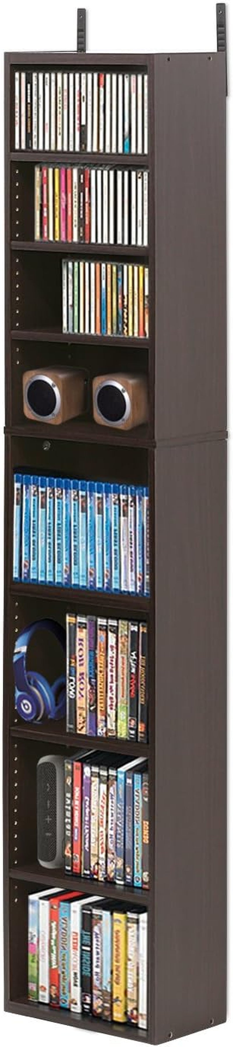 Tall dark-brown slim media tower filled with DVDs, speakers and discs, shown upright from front-right.