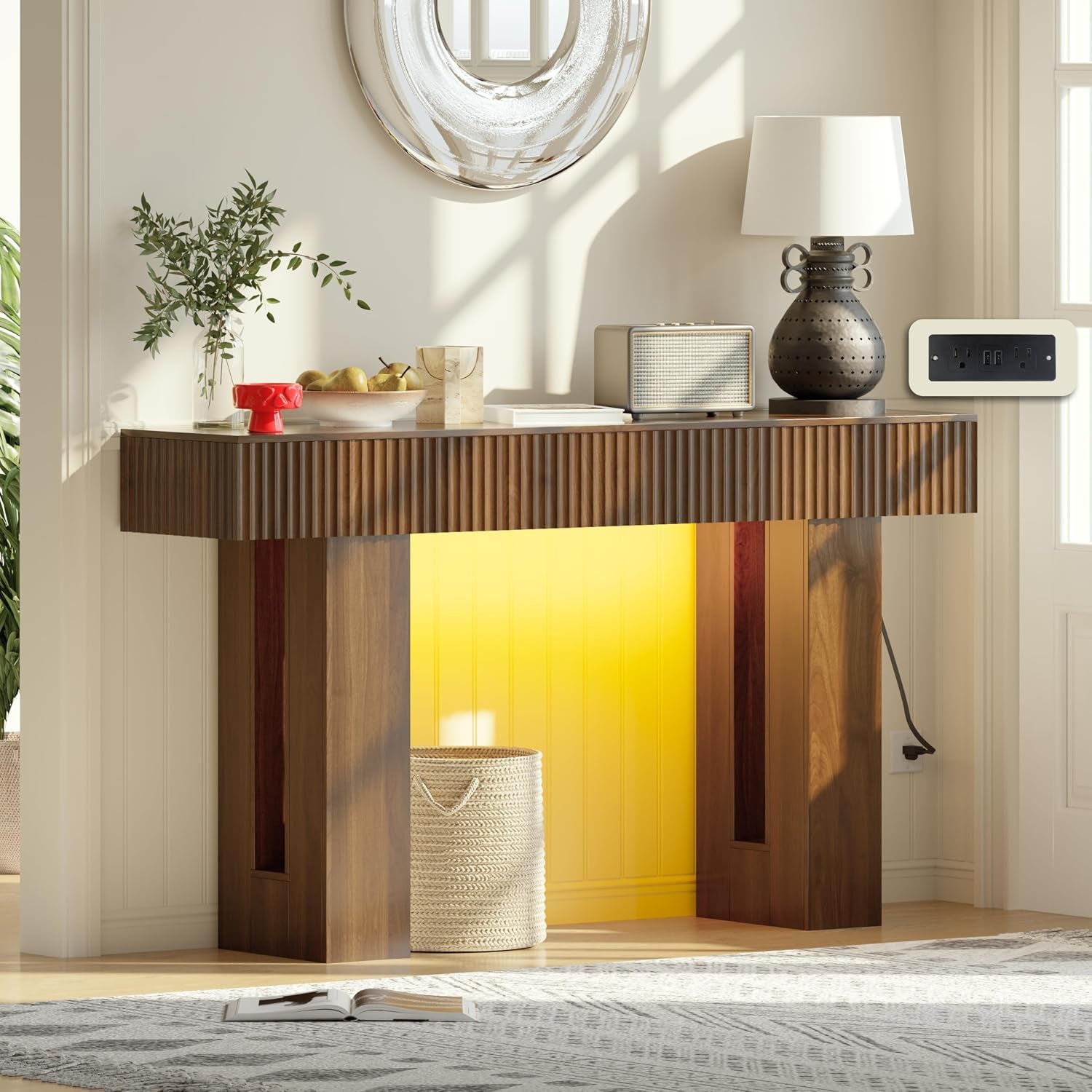 Console table front view with illuminated yellow recessed panel, woven basket underneath, lamp and decorative items on top.