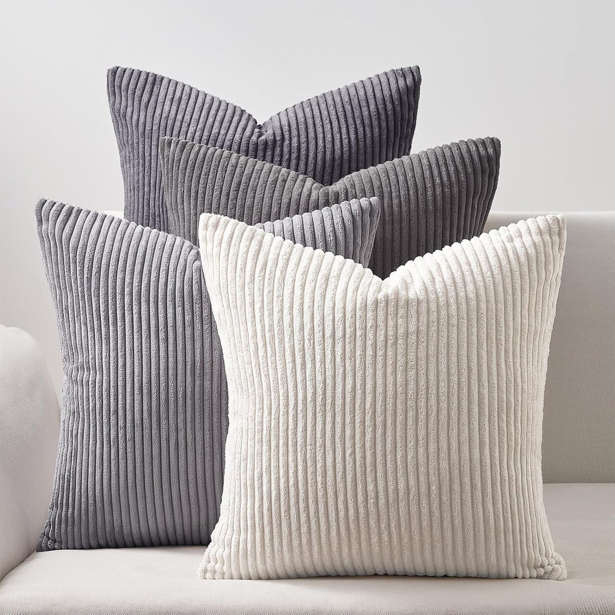 Four ribbed corduroy square pillows in neutral gray and cream tones on a light sofa