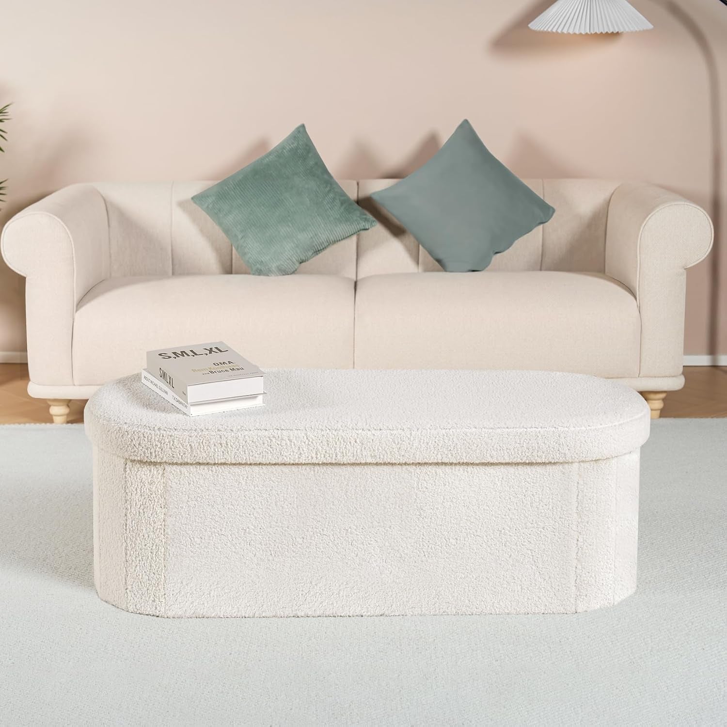 Front-facing ottoman covered in cream sherpa fabric placed on a light rug before a sofa