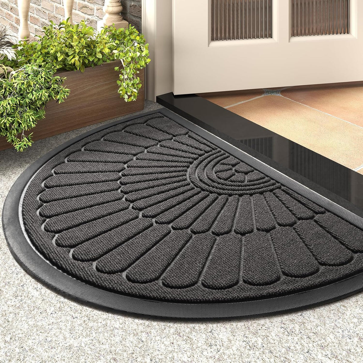 Close-up of a dark gray semicircular mat at a doorway, showing the raised petal pattern and beveled rubber border.