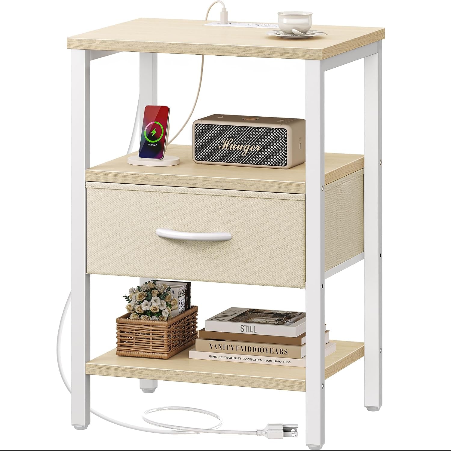 Three-tier nightstand with light wood surfaces, white metal frame and beige fabric drawer, staged with charger and basket.