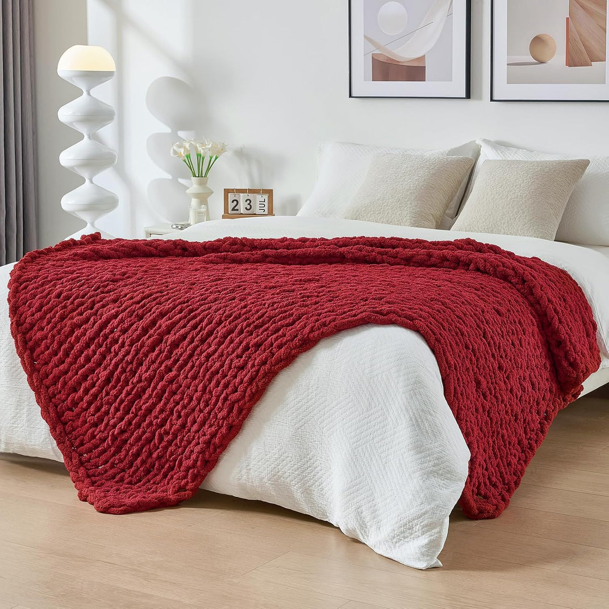 Deep red chunky knit throw laid across the end of a neatly made white bed.