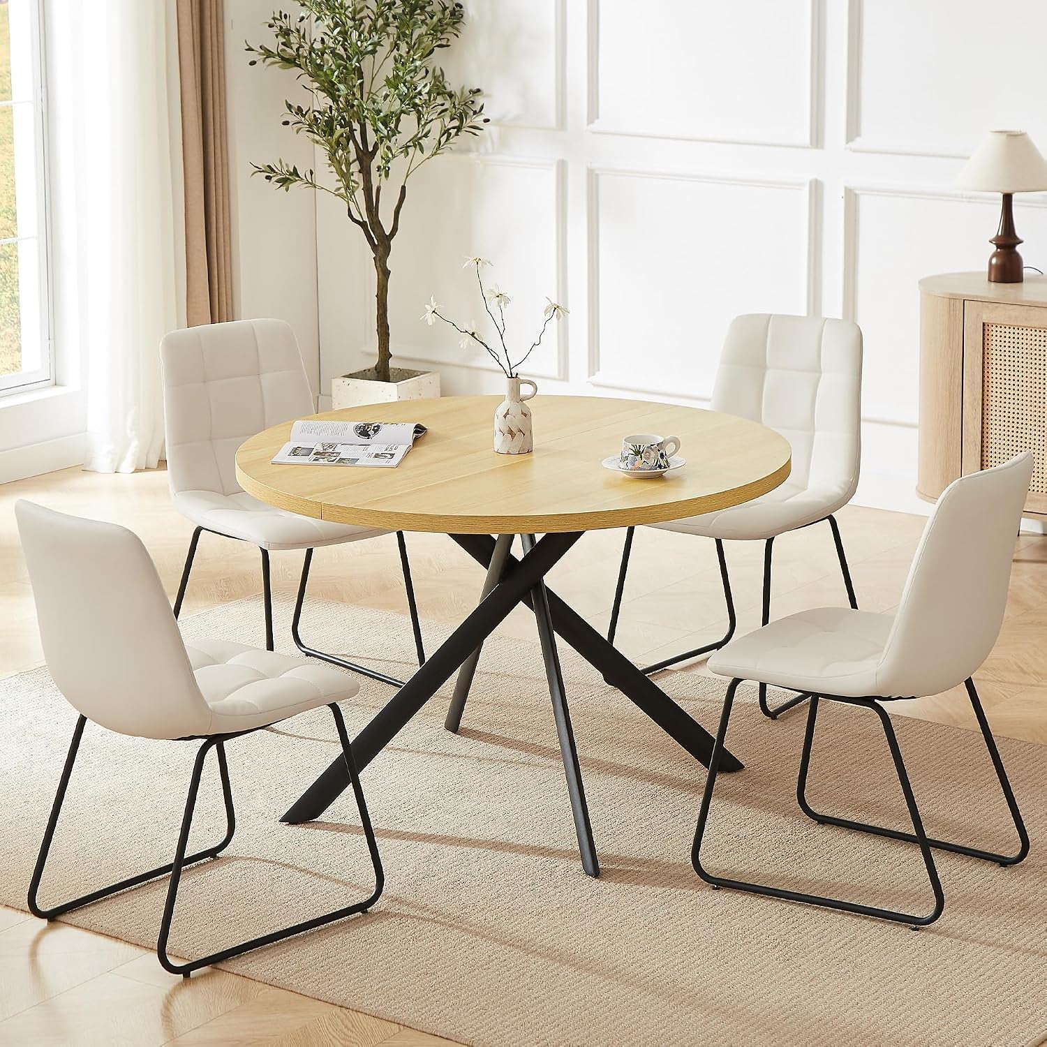 Round dining table with four white quilted chairs and black metal bases in a bright dining space