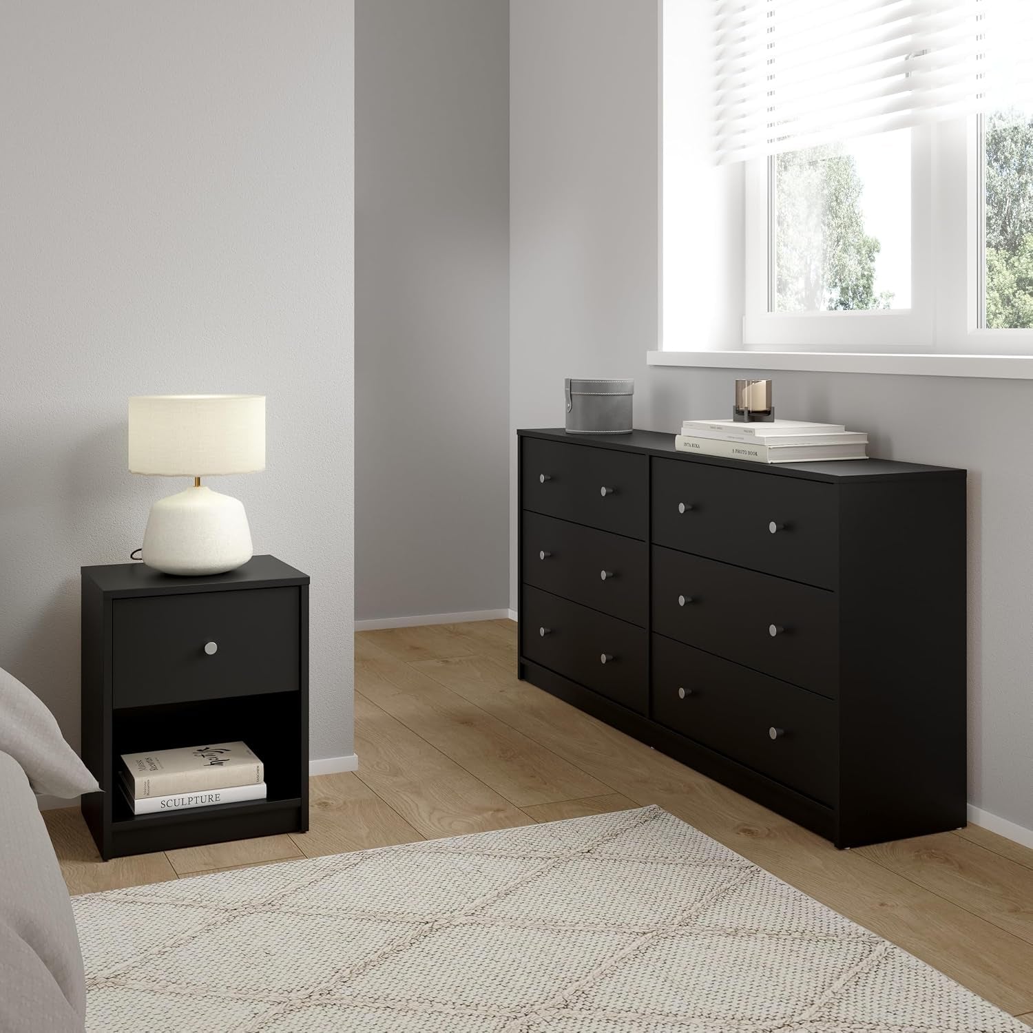 Black nightstand beside a bed and the matching six-drawer dresser under a window in a staged bedroom