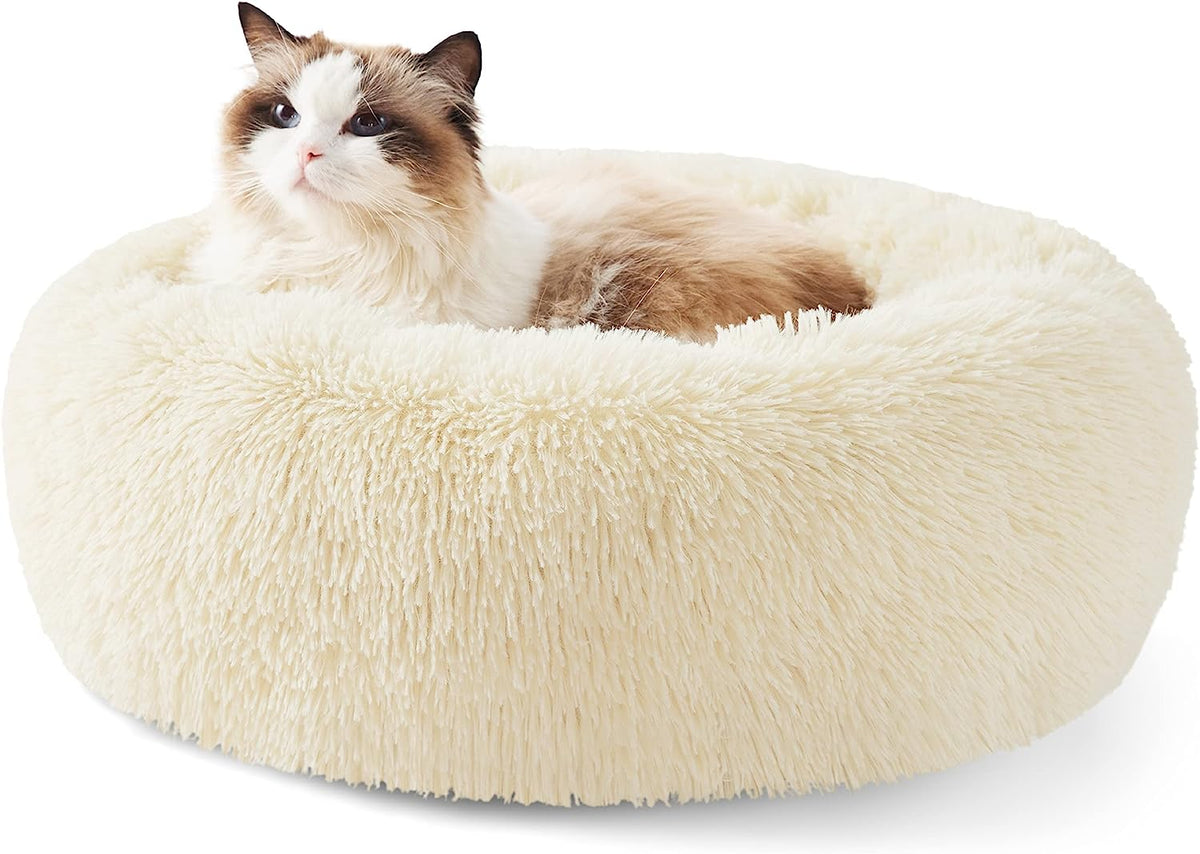 Front view of a cream-colored round faux-fur donut pet bed with a long-haired cat lounging inside.