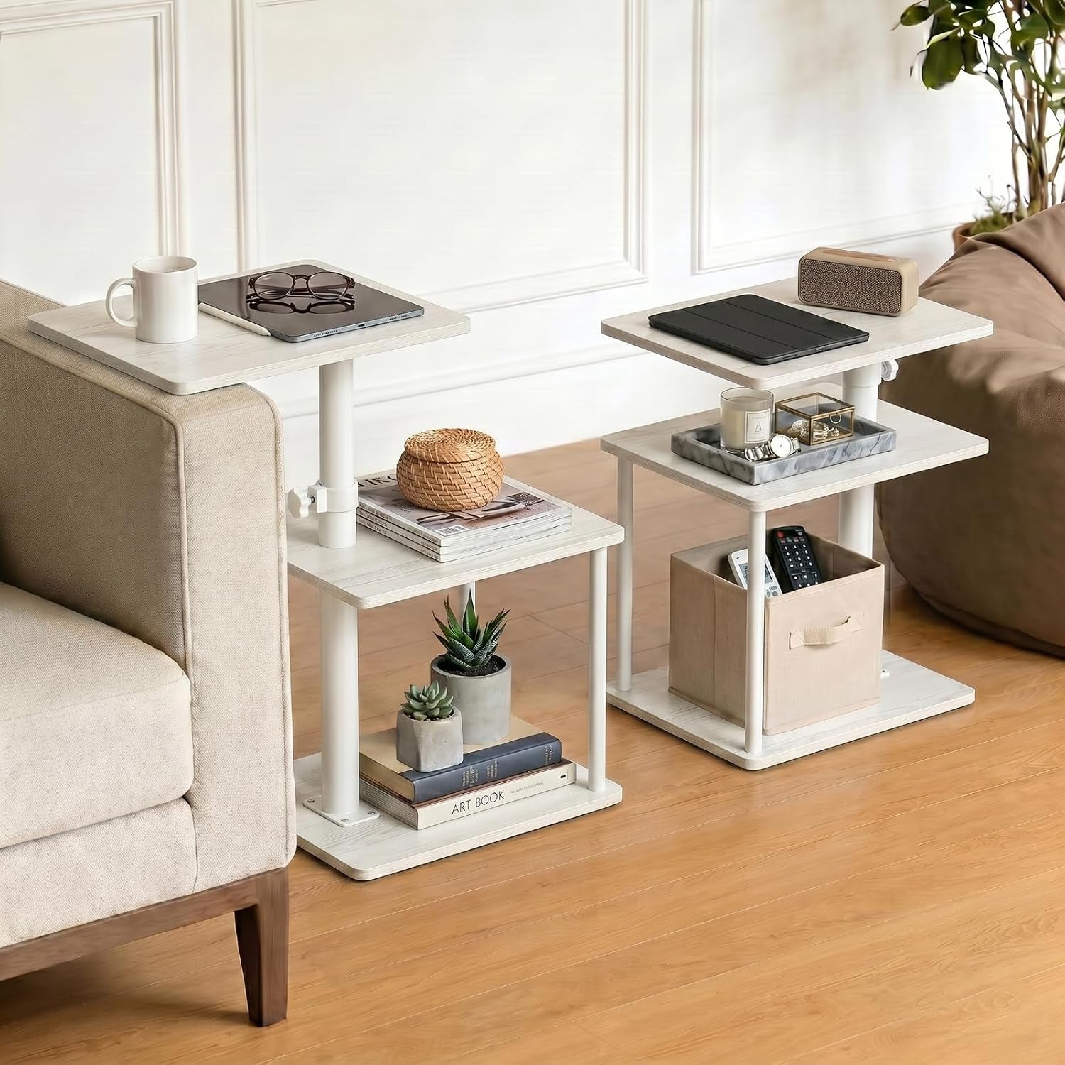 Two white three-tier C-shape side tables styled beside a sofa with decor and storage box.