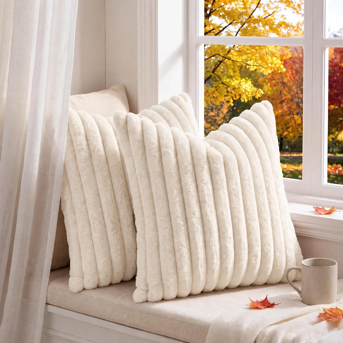Two cream ribbed faux-fur pillow covers on a window seat with autumn leaves and a mug
