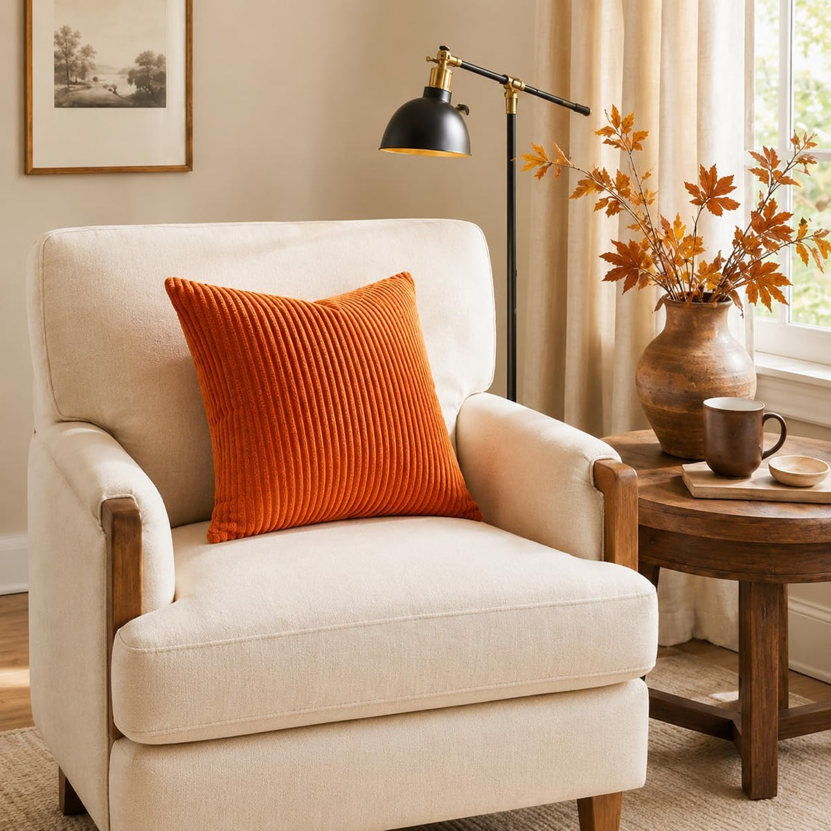 Single orange corduroy throw pillow cover on a cream armchair next to a wooden side table with a lamp