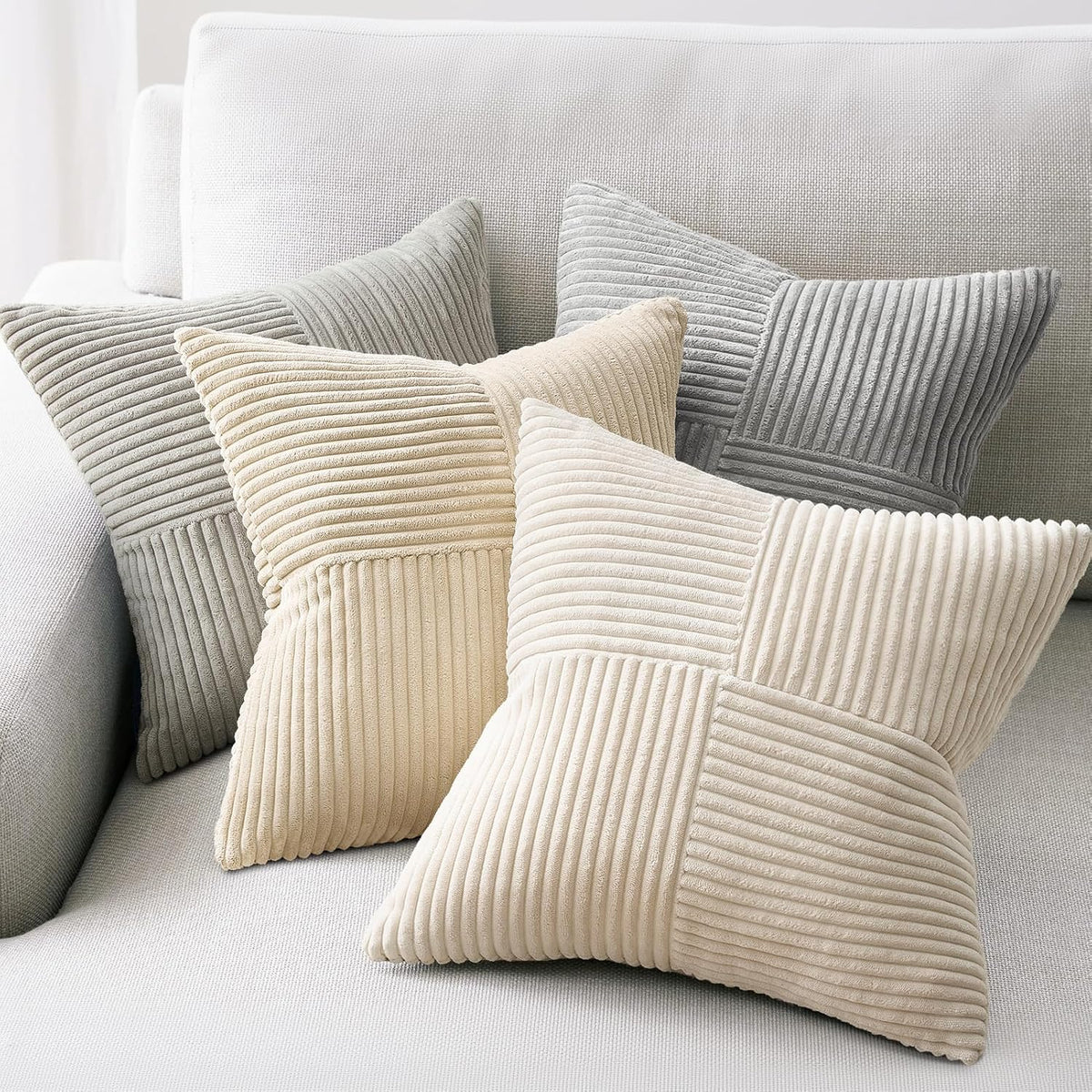 Close grouping of four ribbed square pillow covers in cream, pale yellow, light gray and medium gray on a light sofa.