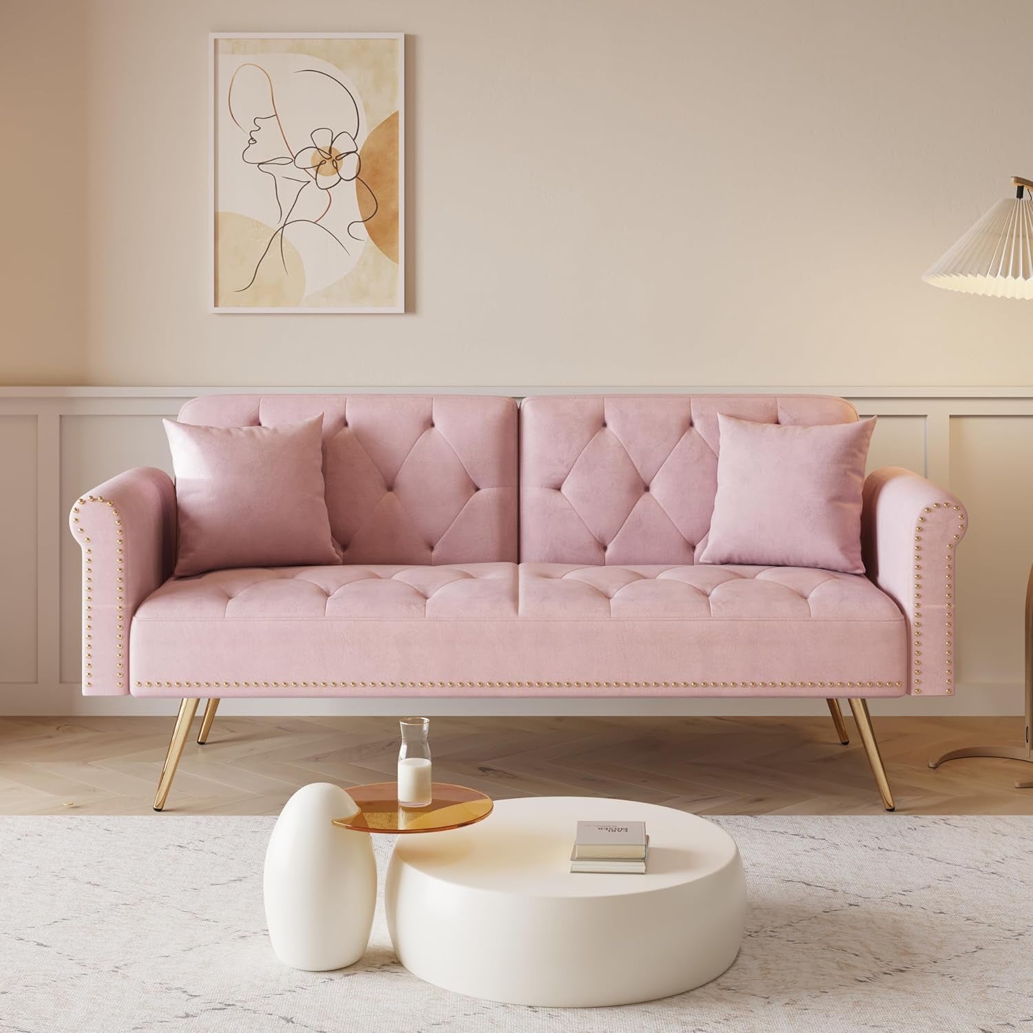 Front view of a pink tufted velvet sofa with nailhead trim and gold legs in a softly lit room.