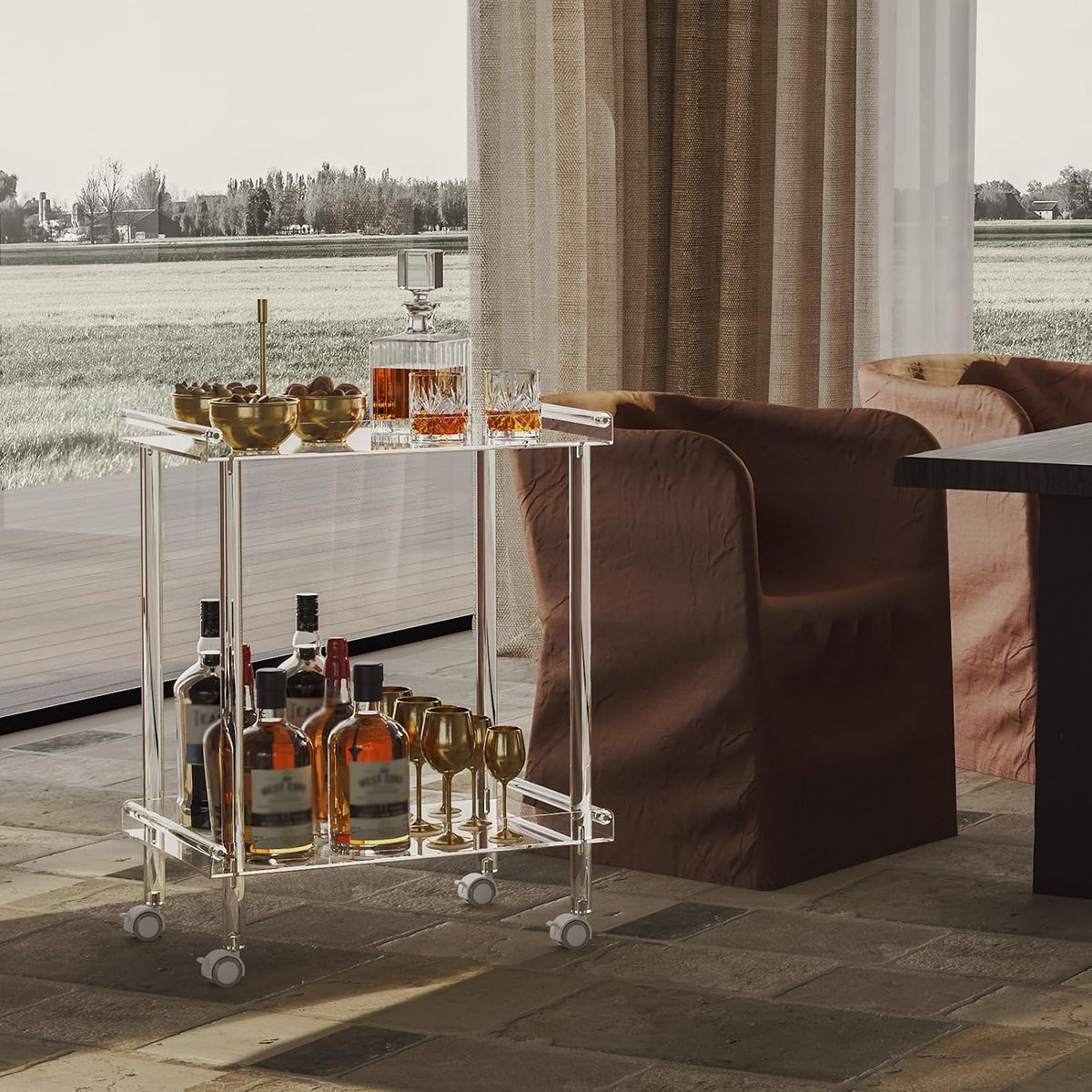 Clear acrylic 2-tier cart beside a dining table and window with liquor bottles on the lower shelf