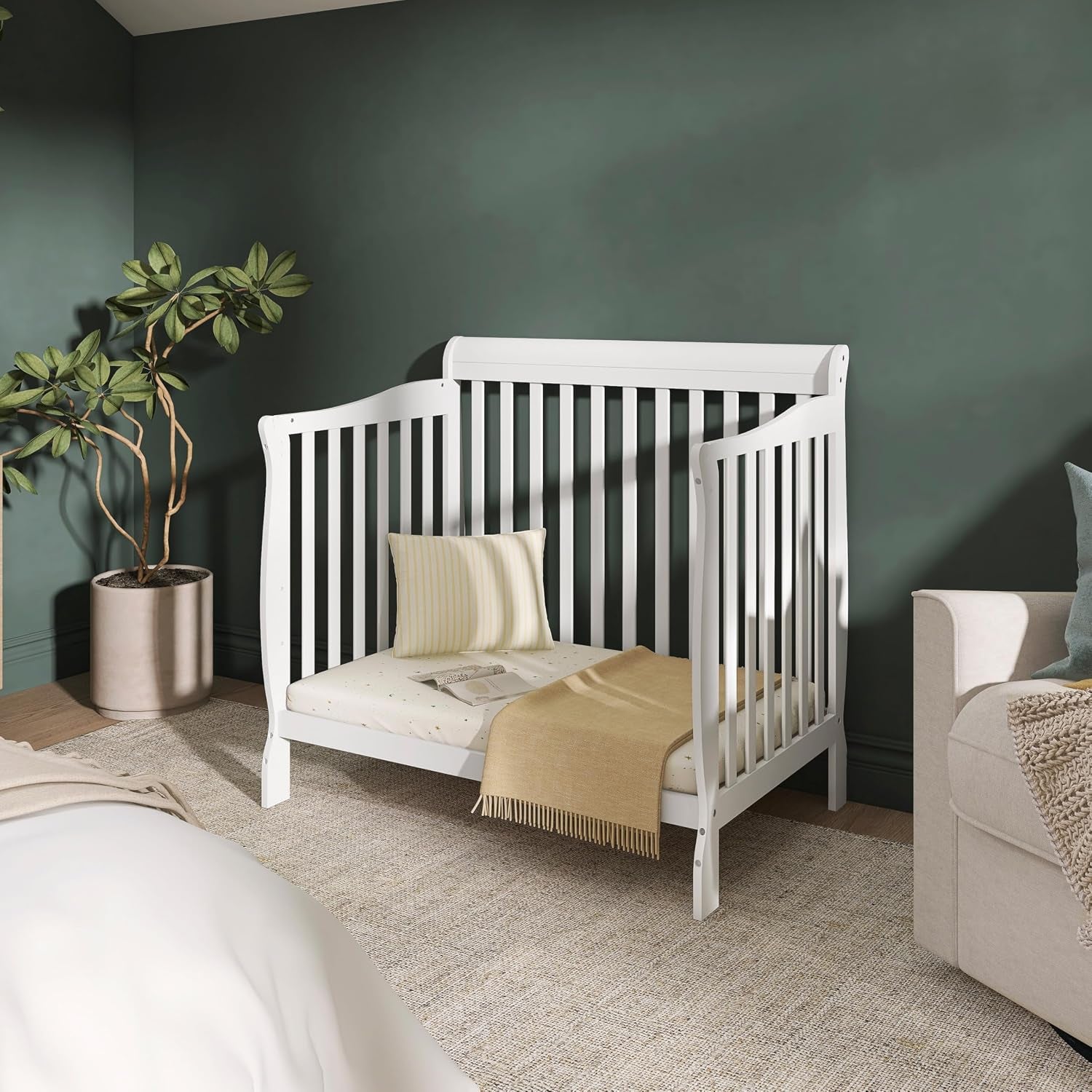 White crib converted to a low toddler bed with a pillow and throw blanket in a cozy bedroom setting.