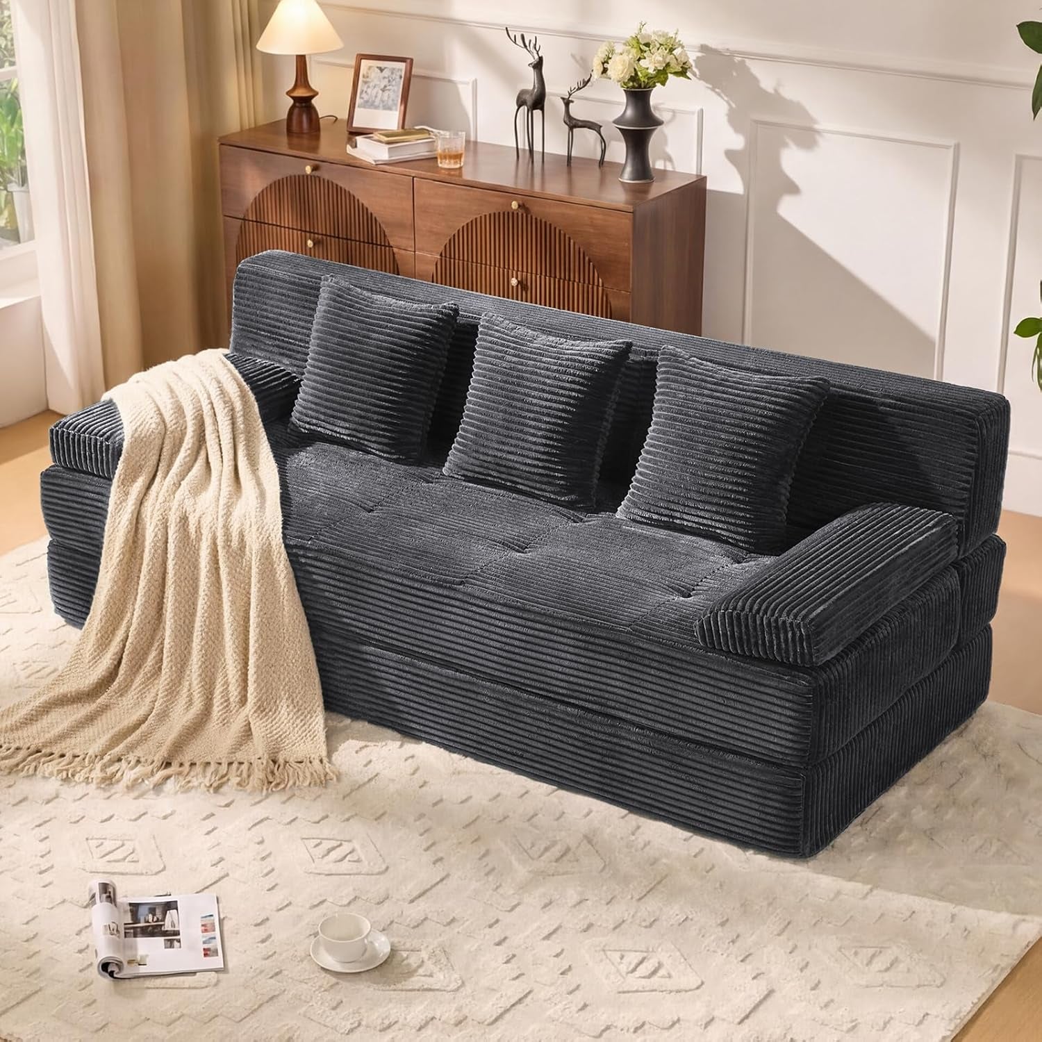 Grey corduroy 3-seat convertible sofa angled front view with three square pillows and throw blanket