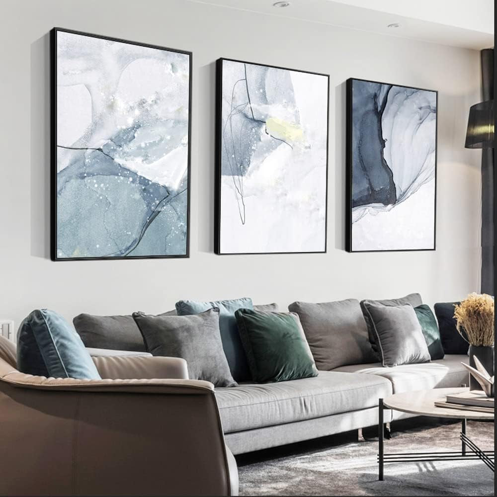 Three framed abstract canvases angled slightly, hanging above a gray sectional sofa in a styled living room