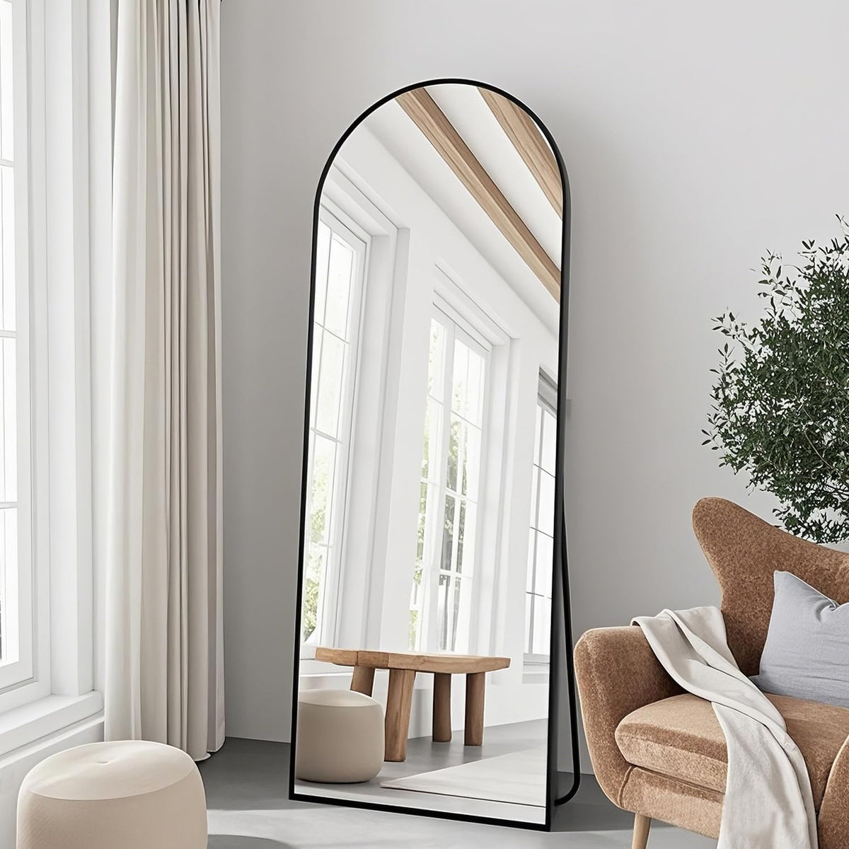 Tall arched full-length mirror with a slim black frame leaning against a wall beside a chair.