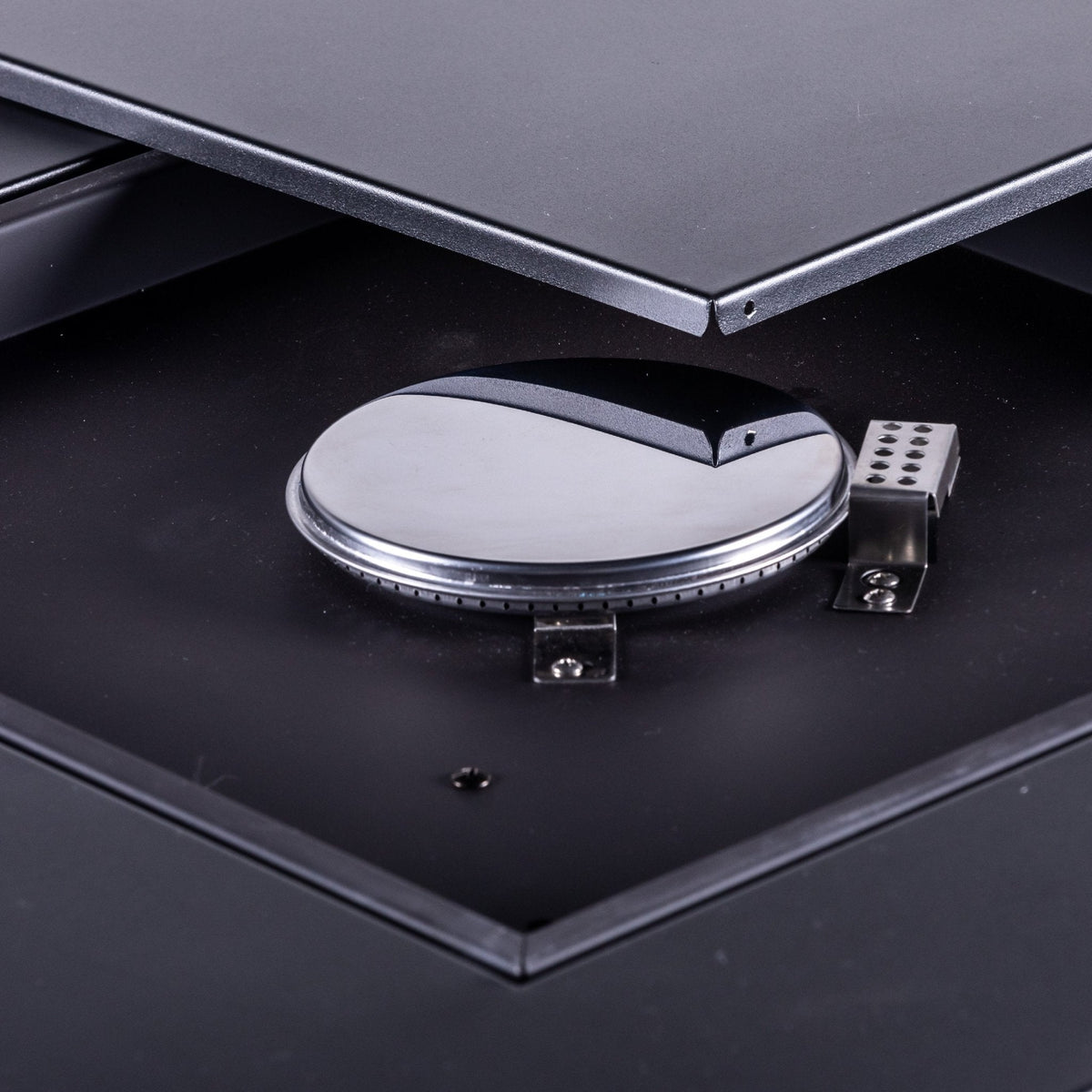 Close-up of a round metal burner and control components beneath a removable tabletop panel.