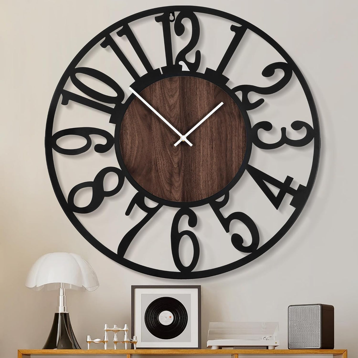 Close front view of the black openwork clock showing white hour and minute hands above a console lamp and framed art